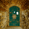 A stone tunnel leads to a dark green door with a curious hex patterned lock. 